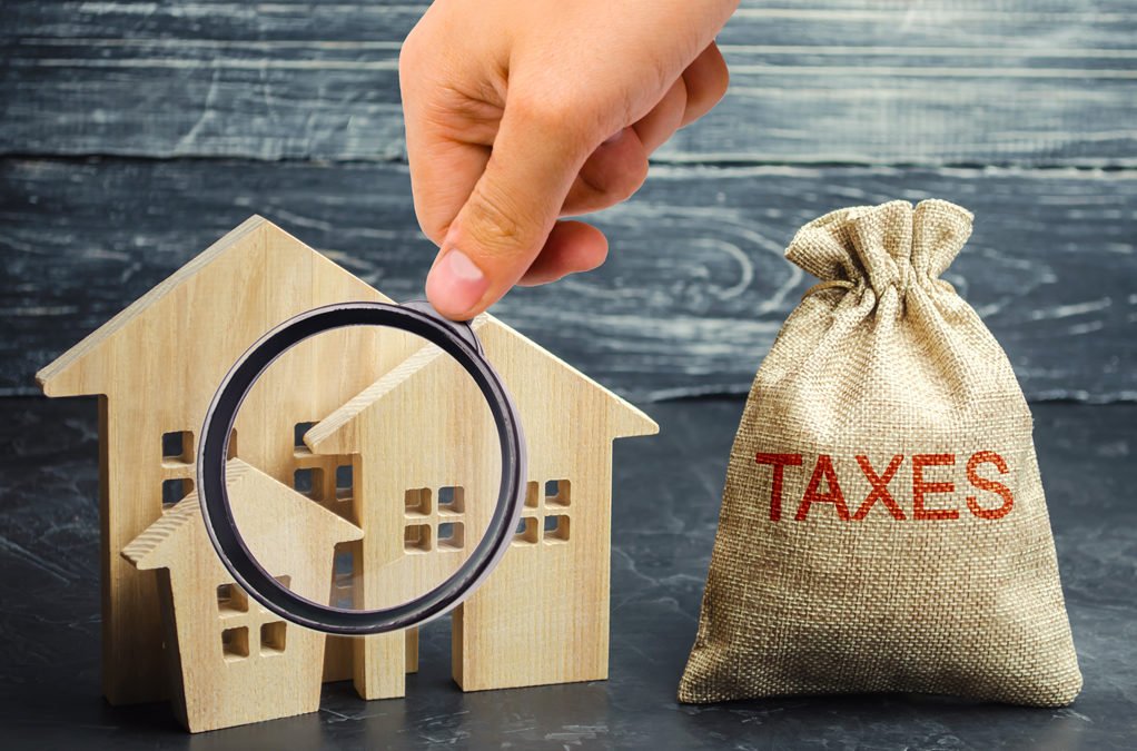 Stamp duty Spain — magnifying glass over wooden house models next to a bag labelled taxes